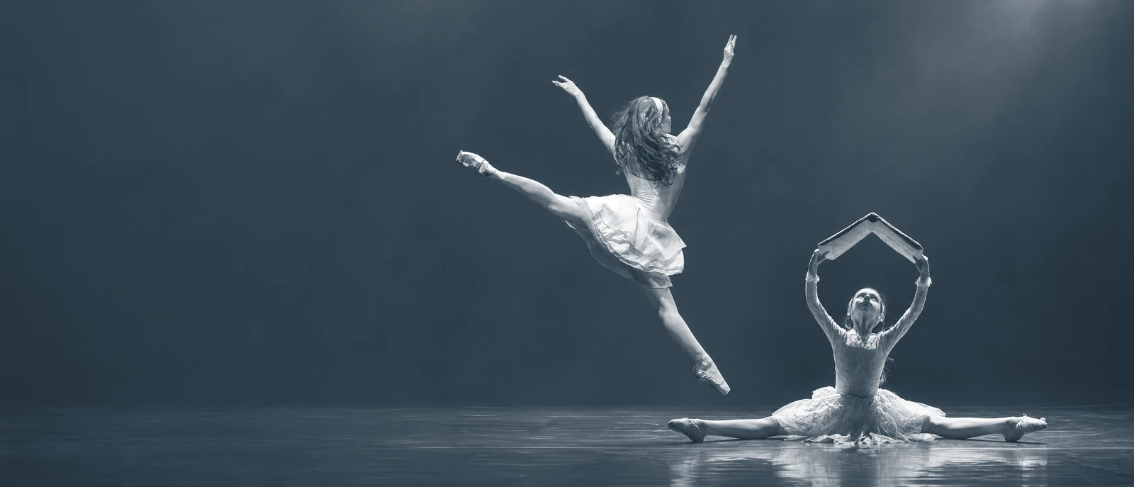 Due giovani danzatrici sul palco: un salto di danza classica e una posa con un libro